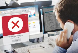Man on phone facing computer with error message on screen.
