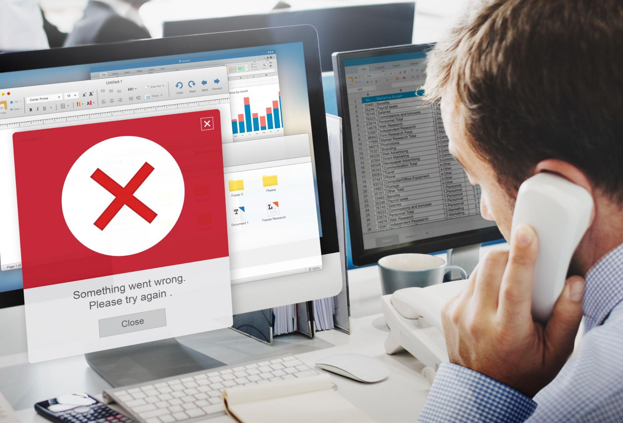 Man on phone facing computer with error message on screen.